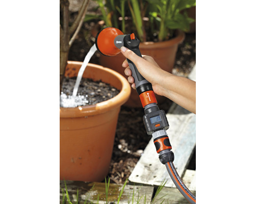 Eine Person bewässert Pflanzen mit einer Gartendusche und einem Wasserzähler.