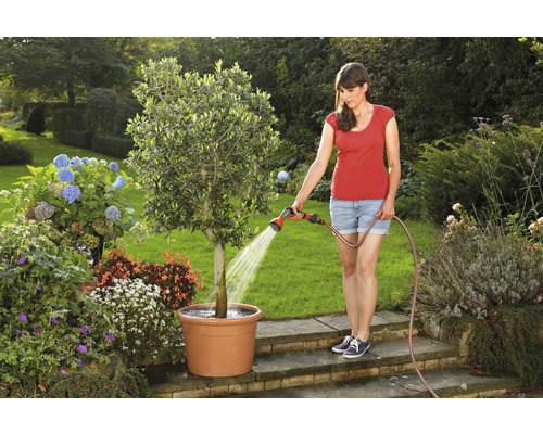 Frau gießt Baum im Topf mit Gartenschlauch im Garten
