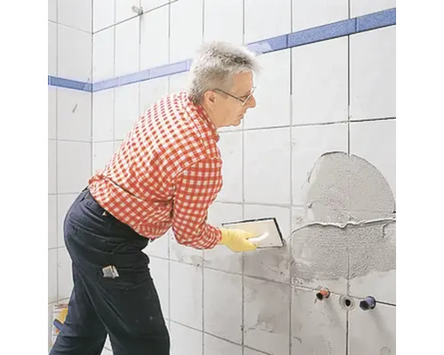 Mann spachtelt eine Wand im Badezimmer mit Fliesenkleber.