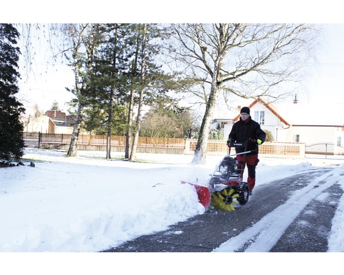 Eine Person bedient eine Schneefräse auf einer schneebedeckten Auffahrt.