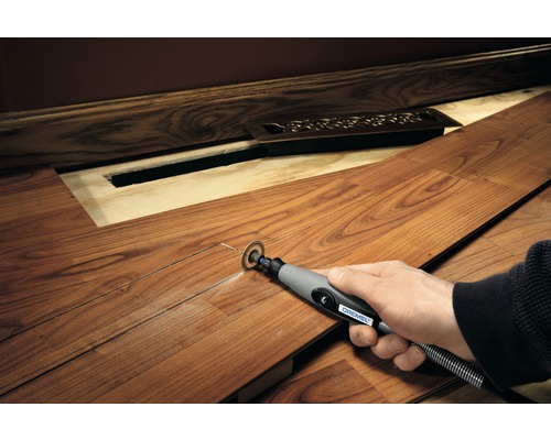 Eine Person schneidet mit einem Dremel Multifunktionswerkzeug ein Laminatbrett zu, um Platz für einen Heizkörper zu schaffen.