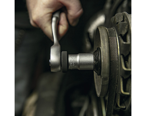 Hand mit Knarre und Steckschlüssel bei der Arbeit an einem Motor