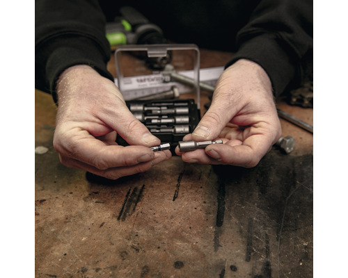 Mann hält magnetischen Bit-Halter und Schrauber-Bit vor einem Bit-Set.