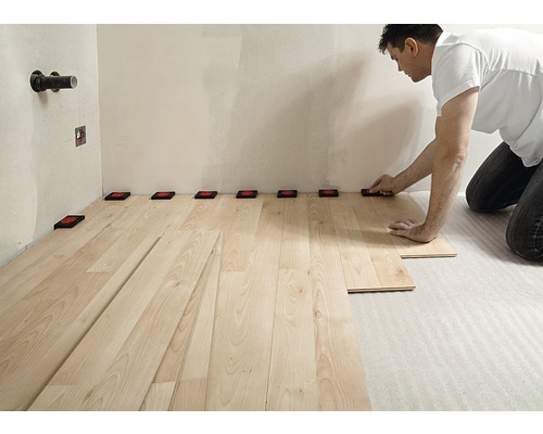 Mann verlegt Laminatboden mit Abstandshaltern an der Wand