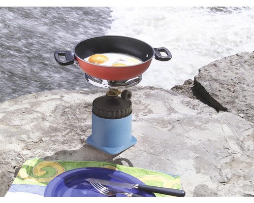 Campingkocher mit Spiegeleiern und Geschirr auf einem Felsen