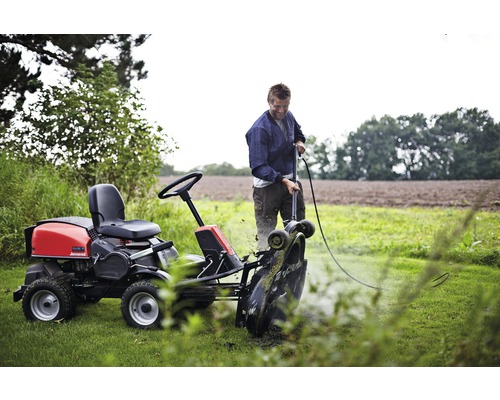 Mann reinigt Rasentraktor auf einer Wiese