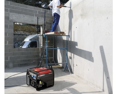 Baustelle mit Honda Stromerzeuger, Bauarbeiter beim Bohren in die Wand stehend auf einem Gerüst