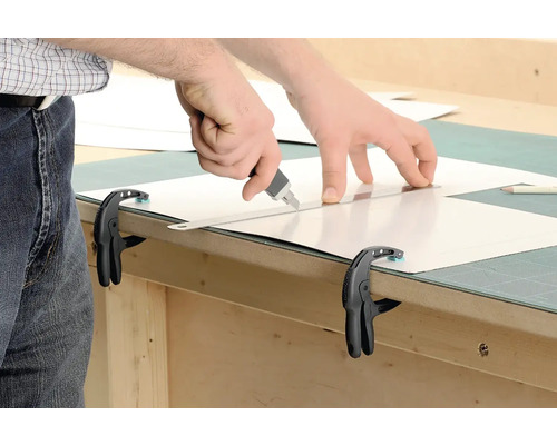 Zuschneiden einer Platte mit einem Cutter an einer Werkbank mit Schraubzwingen fixiert