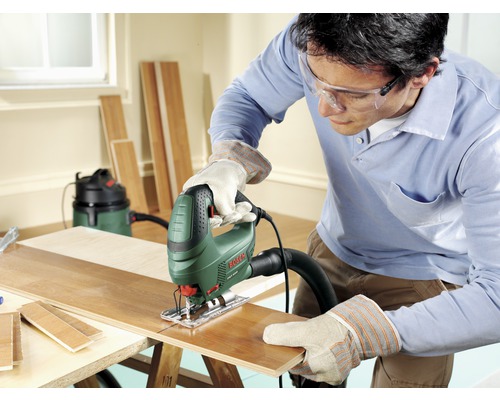 Mann sägt mit einer Stichsäge ein Holzbrett auf einer Werkbank.