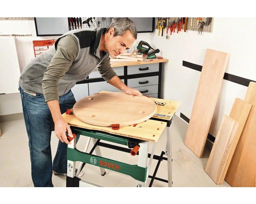 Mann arbeitet mit einer Werkbank an einem runden Holzstück in einer Werkstatt.