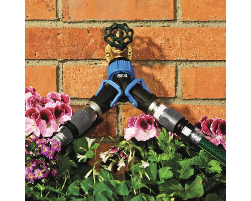 Wasserhahn mit Verteiler und angeschlossenen Gartenschläuchen vor einer Backsteinwand