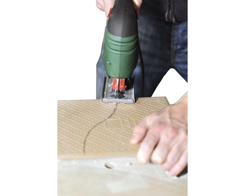 Eine Stichsäge schneidet eine Fliese entlang einer gezeichneten Linie.