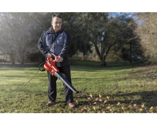 Ein Mann benutzt einen elektrischen Laubbläser im Garten, um Blätter zu entfernen.
