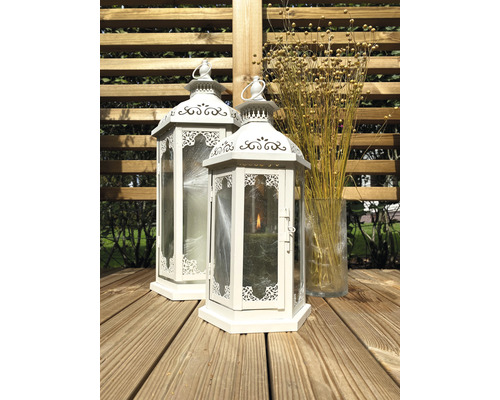 Zwei weiße Laternen aus Metall und Glas auf einer Holzterrasse, daneben eine Glasvase mit trockenen Blumen