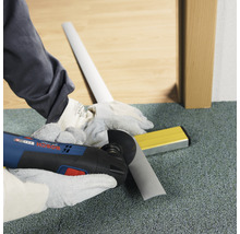 Handwerker schneidet Sockelleiste mit Multifunktionswerkzeug. Wasserwaage liegt bereit.