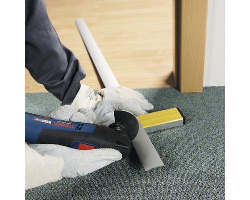 Handwerker schneidet Sockelleiste mit Multifunktionswerkzeug. Wasserwaage liegt bereit.