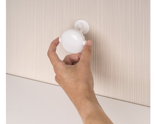 Eine Hand befestigt einen kugelförmigen Möbelriegel an einer Schranktür.