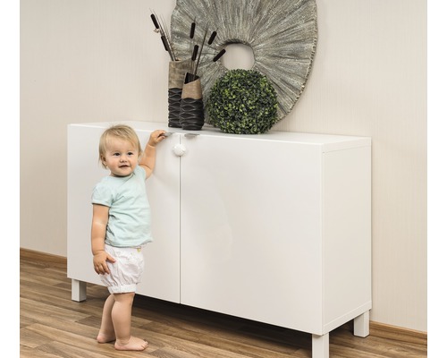 Ein Kind steht neben einem weißen Schrank mit Kindersicherung.