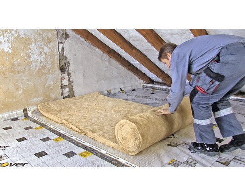 Ein Mann verlegt eine Dämmstoffrolle auf einem Dachboden