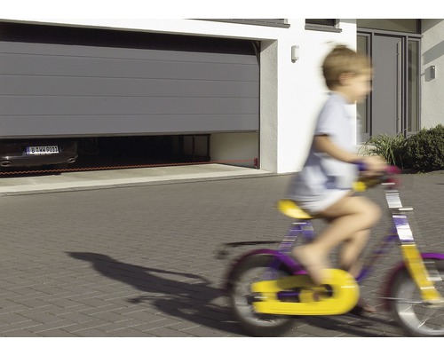 Ein Sektionaltor mit Lichtschranke sichert eine Garage, während ein Kind mit dem Fahrrad vorbeifährt.