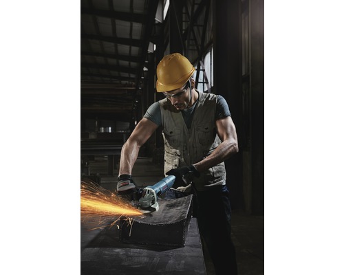 Ein Arbeiter mit Schutzhelm und Schutzbrille verwendet einen Winkelschleifer an einem Metallstück, wodurch Funken entstehen.
