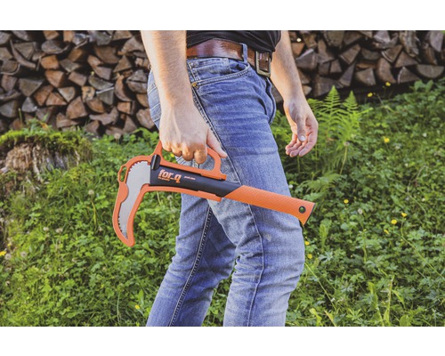 Mann hält eine for_q Axt mit Handschutz vor dem Hintergrund von Holzstapel und Grünfläche.