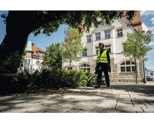 Mann mit Laubbläser reinigt Gehweg vor Gebäude