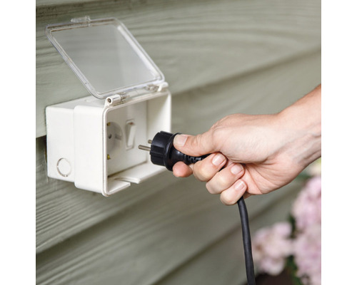 Eine Person steckt einen Stecker in eine wasserdichte Außensteckdose.