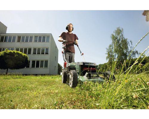 Mann mit Gehörschutz mäht Rasen mit einem Metabo Rasenmäher