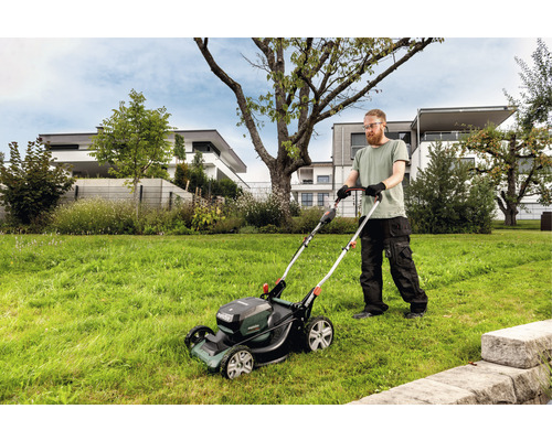Mann mäht Rasen mit einem Akku-Rasenmäher in einem Garten.