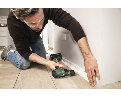 Ein Mann befestigt mit einem Akku-Bohrschrauber eine Fußleiste an der Wand.
