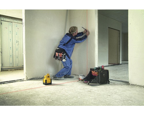 Handwerker markiert Wand mit Laserwasserwaage und Stift in Rohbau