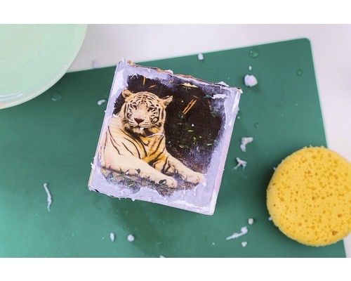 Dekorierte Holzplatte mit Tigerbild, Schwamm und grüner Unterlage.