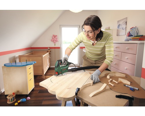 Eine Frau arbeitet mit einer Stichsäge an einem Holzstück in einem Kinderzimmer.