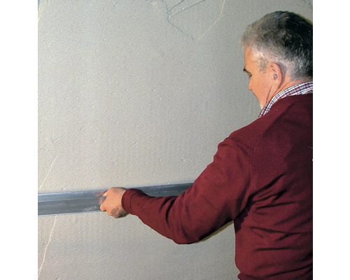 Mann glättet Wand mit Abziehlehre