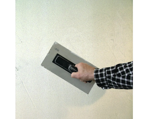 Handwerker glättet Putz mit einer Glättkelle an einer Wand.