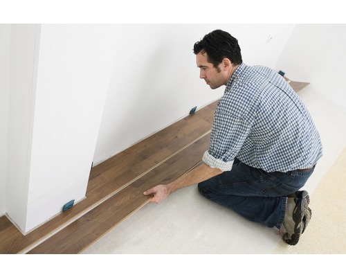 Mann verlegt Laminatboden im Innenraum mit Abstandshaltern.