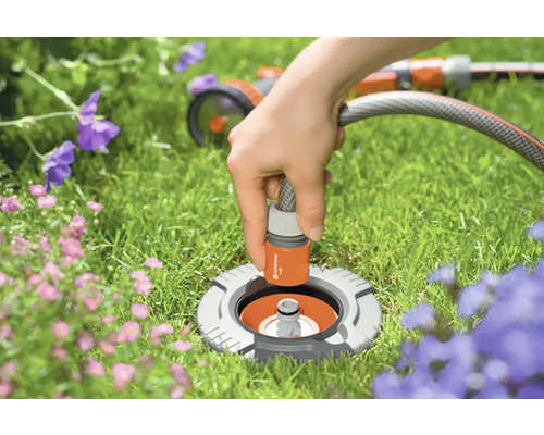 Gartenszene mit versenkter Wassersteckdose und angeschlossenem Gartenschlauch zur Bewässerung