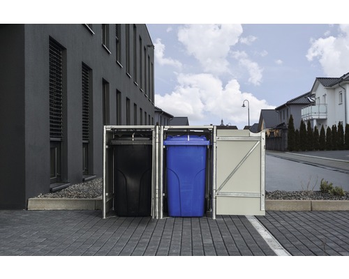 Mülltonnenbox mit drei Mülltonnen auf einem gepflasterten Platz vor einem Gebäude.