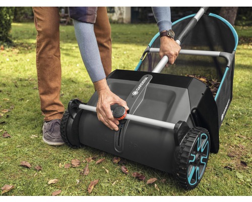 Eine Person bedient einen Laubsammler von Gardena auf einem Rasen mit Laub.