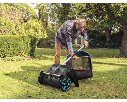 Ein Mann benutzt einen Kehrbesen im Garten, um Laub zu sammeln.