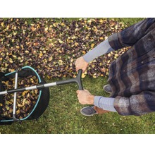 Draufsicht einer Person mit einem Laubsammler auf einer Rasenfläche mit Herbstlaub