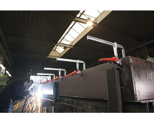 Ein Arbeiter schweißt Metall mit Schraubzwingen in einer Werkstatt.