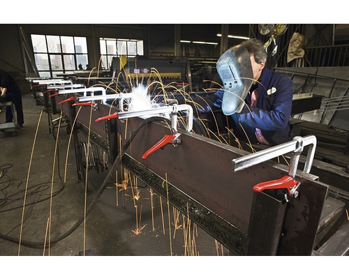 Ein Mann schweißt Metall mit einer Schraubzwinge in einer Werkstatt.