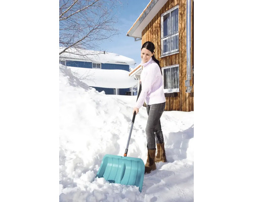 Frau schaufelt Schnee mit einer Schneeschippe vor einem Haus.
