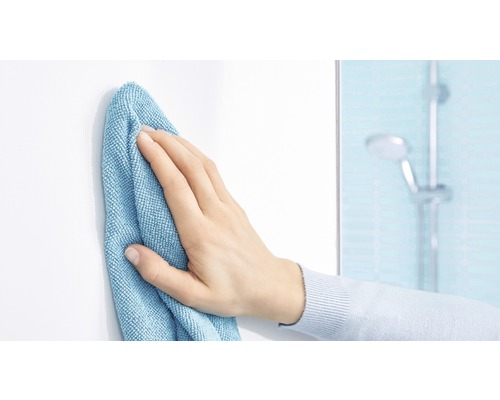 Eine Hand wischt eine weiße Oberfläche mit einem Reinigungstuch in einem Badezimmer.
