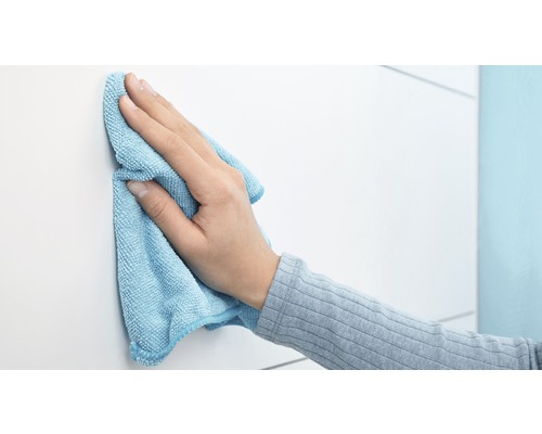 Eine Hand wischt eine weiße Oberfläche mit einem Mikrofasertuch