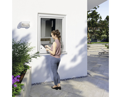 Frau bedient Fenster mit integriertem Bedienelement im Außenbereich eines Hauses.