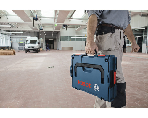 Handwerker trägt Werkzeugkoffer der Marke Bosch in einer Lagerhalle.