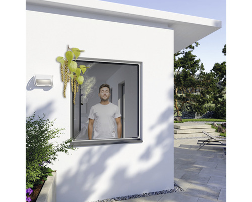 Mann steht am Fenster mit Pollenschutzgitter